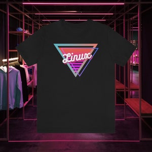 May include: Black t-shirt with a retro design. The design features the word "Linux" in white script inside a colourful triangle. The triangle has gradients of teal, orange, pink, and purple. The t-shirt has a crew neck.