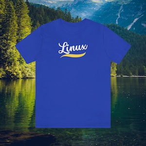 May include: Royal blue t-shirt with the word "Linux" in white script above a yellow curved line. The shirt is displayed against a backdrop of a lake and mountains.