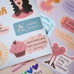 Puede incluir: Un conjunto de pegatinas coloridas con varios diseños y textos. Las pegatinas presentan ilustraciones de una magdalena, un corazón y una mujer con cabello oscuro. El texto en las pegatinas incluye frases como "Legally Anxious", "Made With Love" y "Anxiety Is My Love Language".