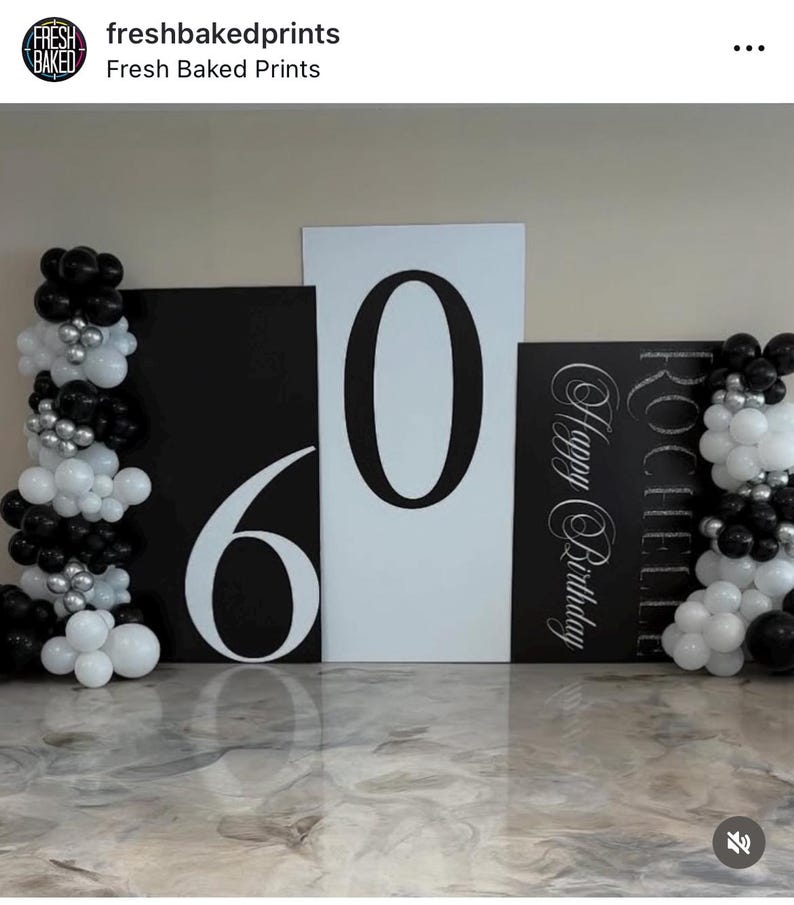 May include: A birthday party decoration set featuring large black and white number cutouts for the number 60. The backdrop includes balloon arrangements in black, white, and silver. The words "Happy Birthday" are also visible.