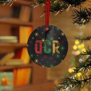 May include: Round Christmas bauble with a black background and white snowflakes. The bauble features the letters "OCR" in red, green, and yellow.