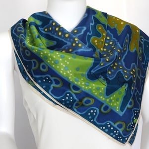 May include: A square silk scarf with a vibrant abstract design. The scarf features a combination of blue, green, and yellow patterns with white accents. The scarf is draped over a mannequin, showcasing its shape and design.