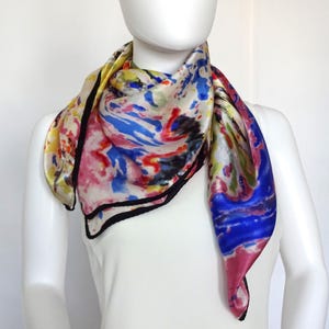 May include: A colorful silk scarf with a black trim. The scarf features a swirling abstract pattern in shades of blue, red, yellow, and pink.