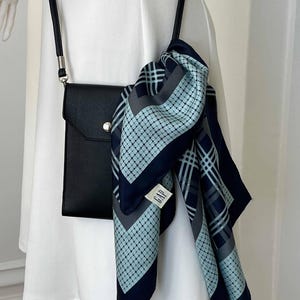 May include: A black crossbody bag with a flap closure and a silver-tone snap. A patterned scarf in navy, light blue, and gray hangs from the bag. The scarf has a geometric design and a tag that reads "GAP".