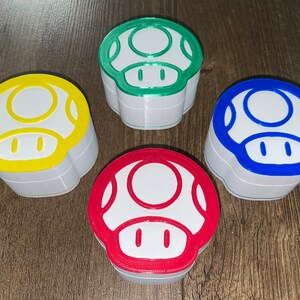 May include: Four mushroom-shaped containers in different colors: green, yellow, blue, and red. Each container has a white top and a white base.