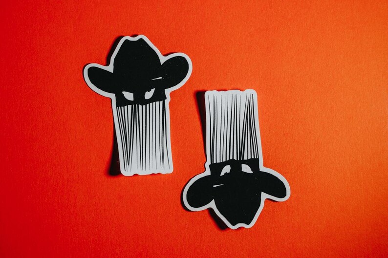 K&ouml;nnte beinhalten: Zwei schwarz-wei&szlig;e Aufkleber einer Person mit Cowboyhut und langem Bart. Die Aufkleber befinden sich auf einem roten Hintergrund.