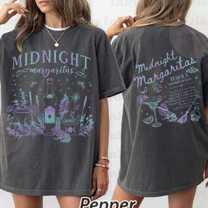 May include: A charcoal gray oversized t-shirt featuring a front graphic with the text Midnight Margaritas, a tequila bottle, a cocktail glass, and a frog. The back graphic displays the text Midnight Margaritas, Tequila Superior Quality, and various botanical and mystical illustrations.