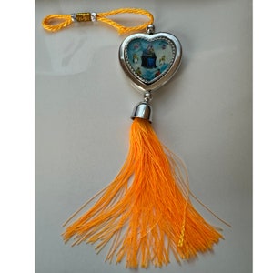 May include: A silver heart-shaped charm with a religious image inside, hanging from a yellow tassel.