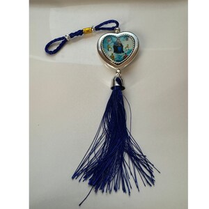 May include: A silver heart-shaped charm with a blue tassel. The charm features a colorful image of a building with people around it.