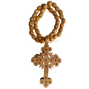 May include: A wooden cross necklace with a detailed design and a string of wooden beads. The cross is a light brown colour and the beads are a slightly darker brown.