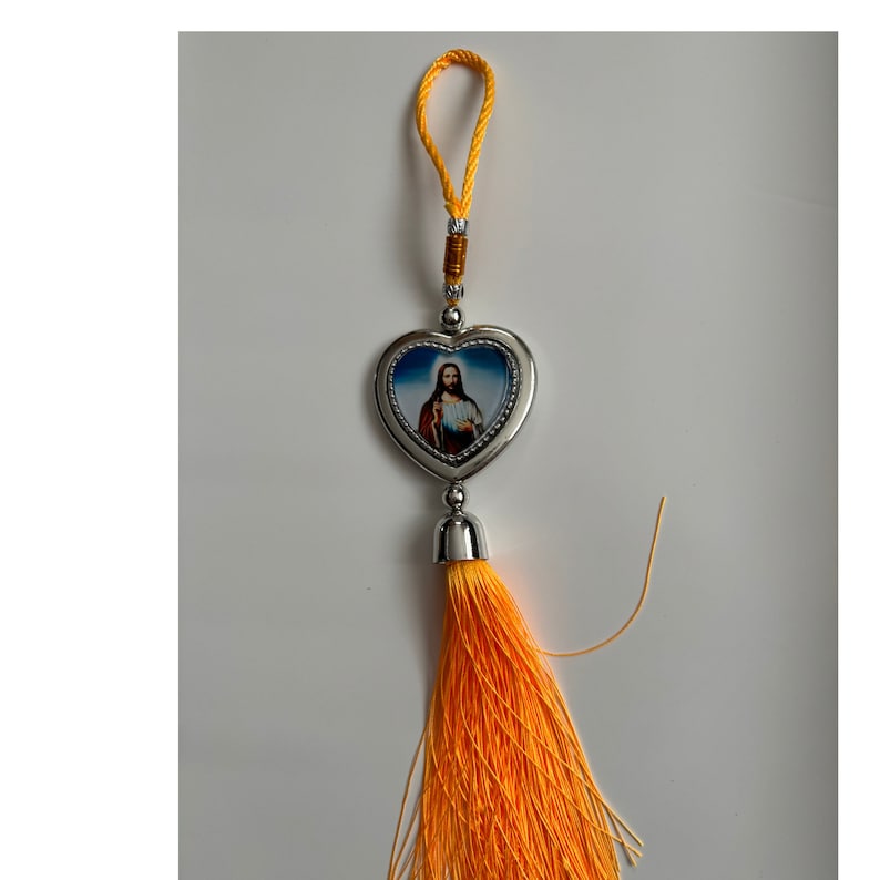May include: A silver heart-shaped charm with a picture of Jesus Christ inside. The charm is attached to a yellow tassel.