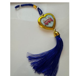 May include: A gold heart-shaped charm with a blue tassel. The charm features a colorful image of people inside. The charm is attached to a blue cord with gold beads.