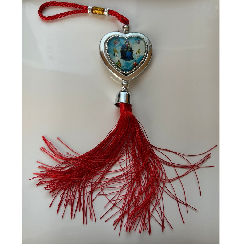 May include: A silver heart-shaped charm with a colorful image inside, hanging from a red tassel. The charm is attached to a red cord with a silver bead.