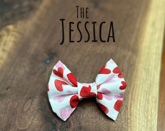 Könnte beinhalten: Ein weißer Fliege mit einem roten und rosa Herzmuster. Die Fliege hat den Text "THE JESSICA" darüber gedruckt.