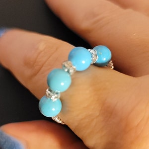 May include: A turquoise beaded ring with silver accents. The ring is worn on a finger.