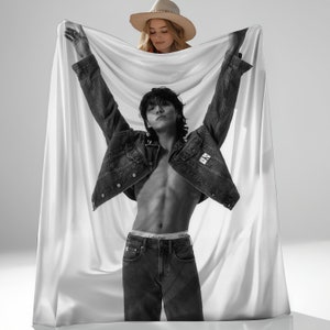 May include: Black and white image of a person wearing a denim jacket and jeans, with arms raised. The person is holding a white blanket. A woman wearing a straw hat is holding the blanket above the person. The Calvin Klein logo is visible on the jacket and underwear.