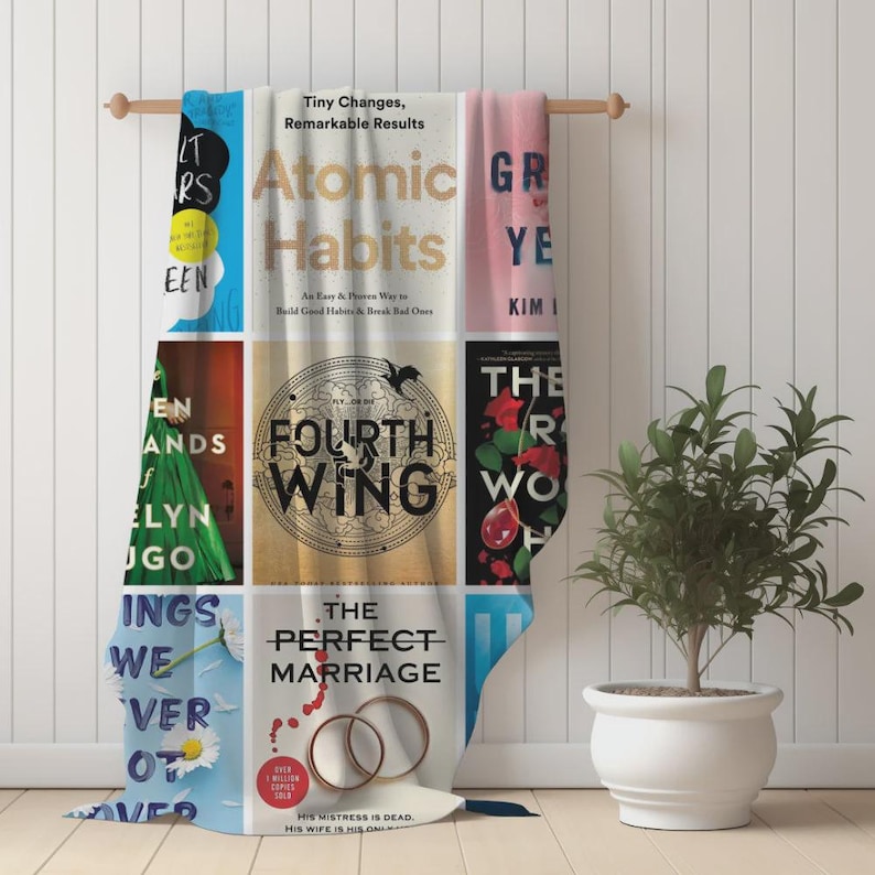 Puede incluir: Una manta decorativa con portadas de libros, incluyendo "Atomic Habits" y "Fourth Wing". La manta es principalmente blanca, con portadas de libros coloridas dispuestas en un patr&oacute;n de cuadr&iacute;cula. El texto "Tiny Changes, Remarkable Results" es visible.