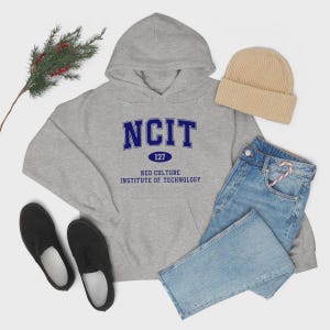 Puede incluir: Una sudadera con capucha gris con el texto azul "NCIT 127 NEO CULTURE INSTITUTE OF TECHNOLOGY". La imagen también incluye un gorro beige, vaqueros azules, zapatillas negras y una ramita verde.