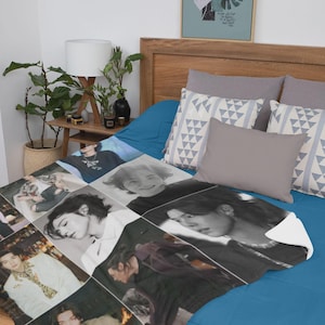 May include: A soft, white blanket featuring a collage of black and white and color photographs of a person. The blanket is displayed on a blue bed with gray pillows and a framed art print.