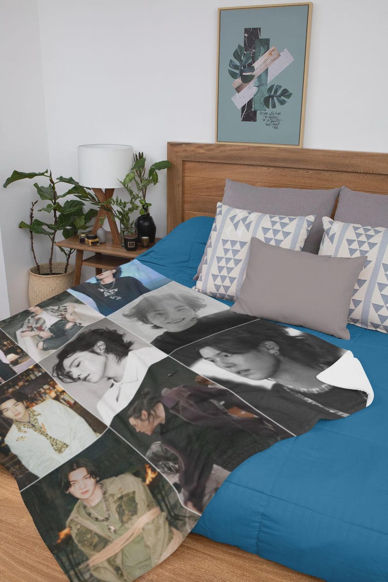 May include: A soft, white blanket featuring a collage of black and white and color photographs of a person. The blanket is displayed on a blue bed with gray pillows and a framed art print.