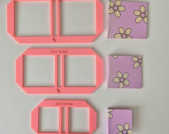 Pode incluir: Três molduras de plástico rosa de tamanhos diferentes para fazer álbuns de fotos. As molduras são etiquetadas com as medidas 80 x 80 mm, 70 x 70 mm e 45 x 55 mm.