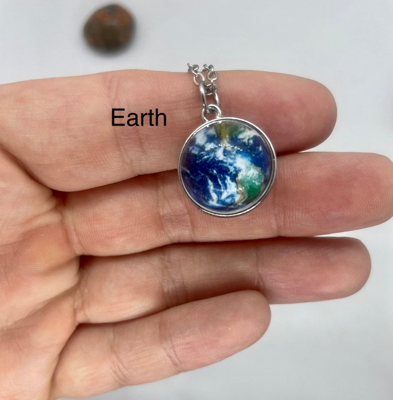 May include: A silver chain necklace with a round pendant featuring a detailed image of Earth. The pendant has a silver border and a blue, green, and white image of the planet.
