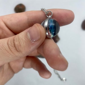 May include: A silver chain necklace with a round pendant featuring a colorful, abstract design encased in clear resin.