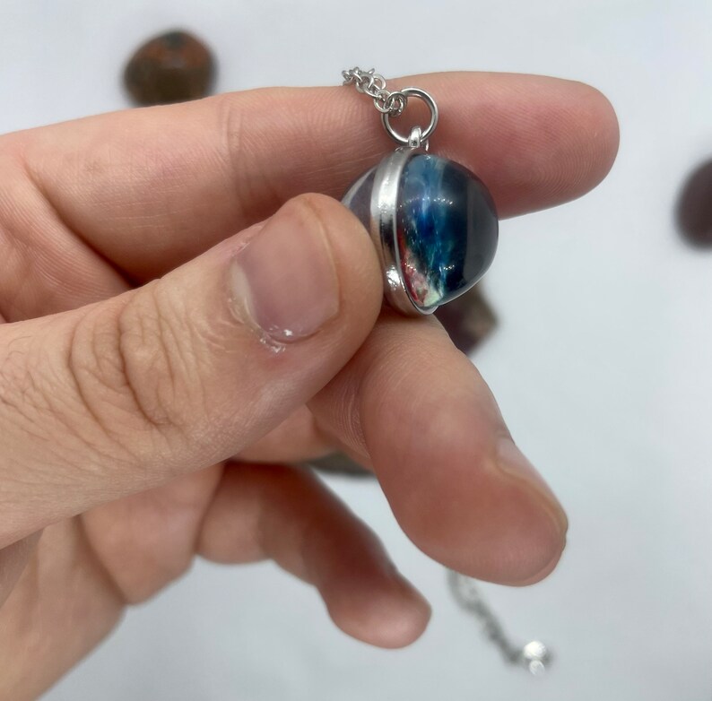 May include: A silver chain necklace with a round pendant featuring a colorful, abstract design encased in clear resin.