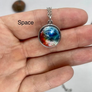 May include: A silver chain necklace with a round pendant featuring a colorful galaxy image. The pendant is surrounded by a silver frame. The text "Space" is visible in the image.