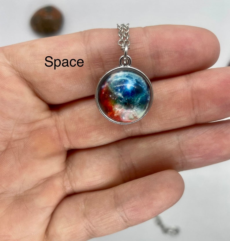 May include: A silver chain necklace with a round pendant featuring a colorful galaxy image. The pendant is surrounded by a silver frame. The text "Space" is visible in the image.