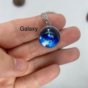 May include: A silver chain necklace with a round glass pendant featuring a galaxy image. The pendant has a silver rim.