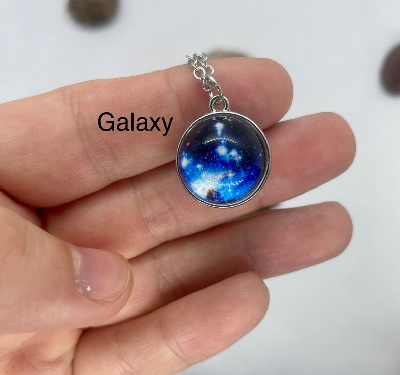 May include: A silver chain necklace with a round glass pendant featuring a galaxy image. The pendant has a silver rim.