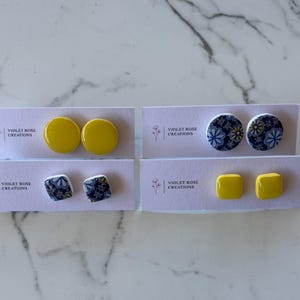May include: Four pairs of earrings displayed on white cards with the text "Violet Rose Creations". The earrings are made of ceramic and feature yellow and blue floral patterns.