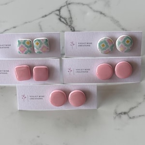 May include: Six pairs of pink and white polymer clay earrings. The earrings are displayed on white cards with the text "Violet Rose Creations".