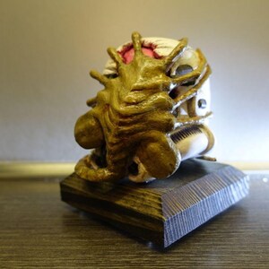 May include: A golden alien creature figurine bursting out of a white skull, mounted on a dark wood base.