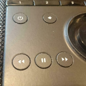 Könnte beinhalten: Nahaufnahme eines schwarzen Lautsprechers mit einem Bedienfeld mit Knöpfen für Strom, Rückspulen, Wiedergabe/Pause, Vorspulen und einem runden Knopf.