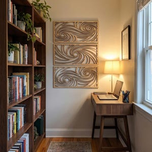 Könnte beinhalten: Drei Wandkunstpaneele aus Holz mit einem Wirbeldesign werden an einer hellen Wand ausgestellt. Unter der Kunst befindet sich ein Holzschreibtisch mit einem Laptop und einer Lampe. Auf der linken Seite befindet sich ein Bücherregal voller Bücher und Pflanzen.