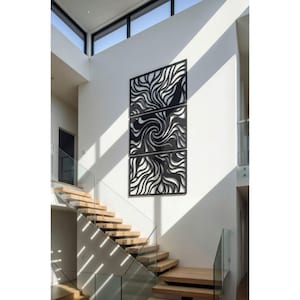 May include: A modern, black metal wall art installation composed of three rectangular panels. Each panel features a flowing, abstract design of swirling lines and curves, creating a dynamic visual effect. The artwork is mounted on a white wall.