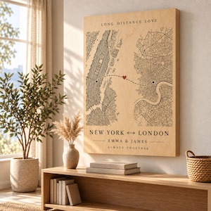 Puede incluir: Un cuadro rectangular de madera con dos mapas de ciudades en tinta negra conectados por una línea discontinua con un pequeño corazón rojo. El texto dice LONG DISTANCE LOVE, NEW YORK <-> LONDON, EMMA & JAMES y ALWAYS TOGETHER en letras negras.