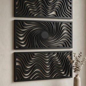 May include: Three black, rectangular wall art panels with intricate wave and spiral designs. The panels are mounted on a neutral-colored wall, creating a modern and artistic display. The panels are made of a dark material, possibly wood or metal.