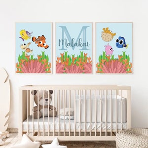 May include: Three framed prints with a blue background and coral reef imagery. The first print features a yellow fish, a turtle, and an orange and white clownfish. The second print features the letter M and the name Malakai. The third print features a pufferfish, a blue tang, and a pink fish.