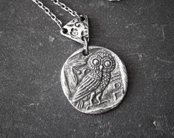 May include: Silver necklace with an owl pendant. The owl is depicted in a detailed, antique style, with large eyes and intricate feathers. The pendant is attached to a silver chain.