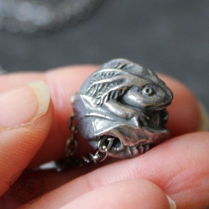 May include: A silver charm necklace featuring a detailed frog sculpture with a leafy design. The frog is curled up in a protective pose, with its eyes closed.