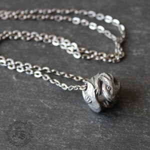 May include: A silver chain necklace with a pendant featuring a detailed sculpture of a small dragon curled up in a ball.
