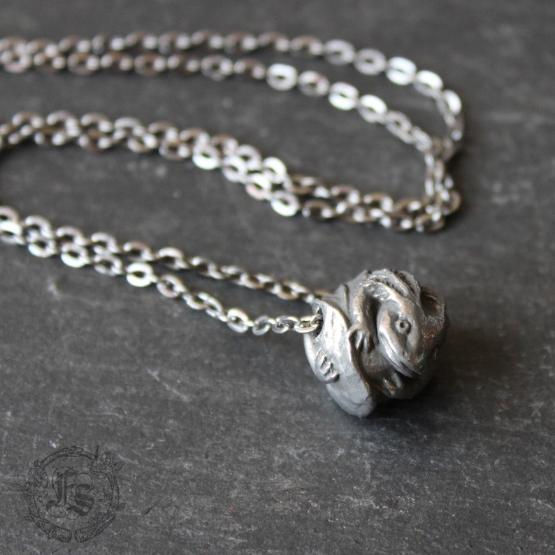 May include: A silver chain necklace with a pendant featuring a detailed sculpture of a small dragon curled up in a ball.