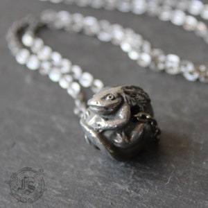 May include: A silver necklace with a detailed, three-dimensional pendant of a frog sitting on a leaf.