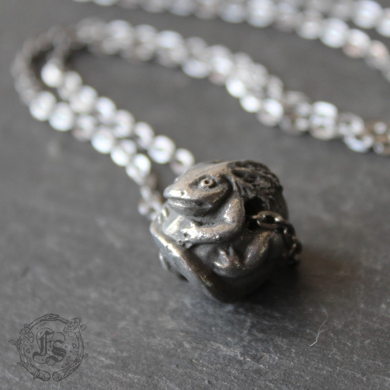 May include: A silver necklace with a detailed, three-dimensional pendant of a frog sitting on a leaf.