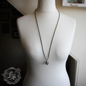 May include: A dark green cord necklace with a silver pendant shaped like a cluster of small spheres.