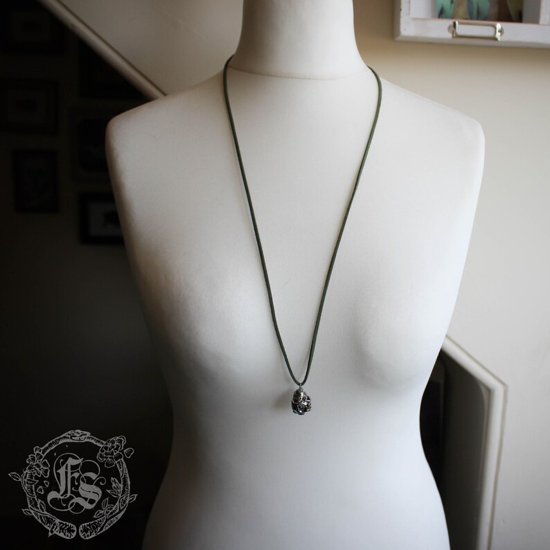 May include: A dark green cord necklace with a silver pendant shaped like a cluster of small spheres.