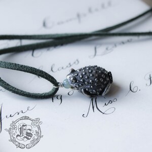 May include: A silver toad pendant with a green gemstone bead on a dark green suede cord.
